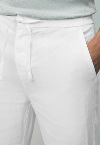White linen trousers featuring a drawstring waist, side pockets, and a textured finish. Comfortable and lightweight fabric ideal for warm weather.
