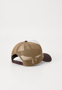 Smeđi mrežasti trucker šešir sa tamnosmešnim čelom i belom prednjom panelom. Ima podesivu traku na poleđini. Tekstura materijala je kroz ceo šešir.