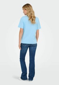Lichtblauwe katoenen t-shirt met korte mouwen, relaxte pasvorm, gezien van achteren, gecombineerd met slim fit blauwe spijkerbroek met een flair en witte sneakers.
