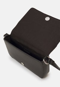 Sort læder crossbody taske med magnetisk lukning, der har en glat overflade, indvendige lommer og en justerbar rem.