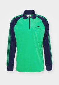 Zelena i mornarsko plava polo majica dugih rukava od mekanog tkanja, s ovratnikom na patentni zatvarač, džepom na prsima i kontrastnim prugastim rukavima.