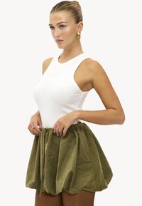 Débardeur blanc côtelé associé à une jupe verte texturée à cordon de serrage, présentant une forme volumineuse et ballon ainsi qu'une taille froncée.