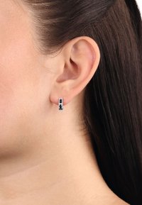 Srebrne kolczyki w kształcie kół z czarnym akcentem. Charakteryzują się eleganckim, geometrycznym wzornictwem oraz polerowanym wykończeniem.