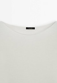 T-shirt blanc, léger, avec un grand col et une texture douce. Présente une petite étiquette noire indiquant la marque et le pays d'origine.