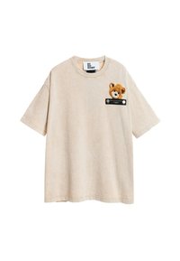 Camiseta de algodón beige con mangas cortas y un escote redondo, que presenta un bordado de un oso de peluche en el lado izquierdo del pecho y una etiqueta negra.