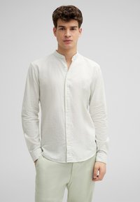 Helles gestreiftes Langarmhemd in hellgrün und creme, aus Baumwollstoff, mit Stehkragen, Knopfverschluss, schmale Passform, kombiniert mit hellgrünen Hosen.