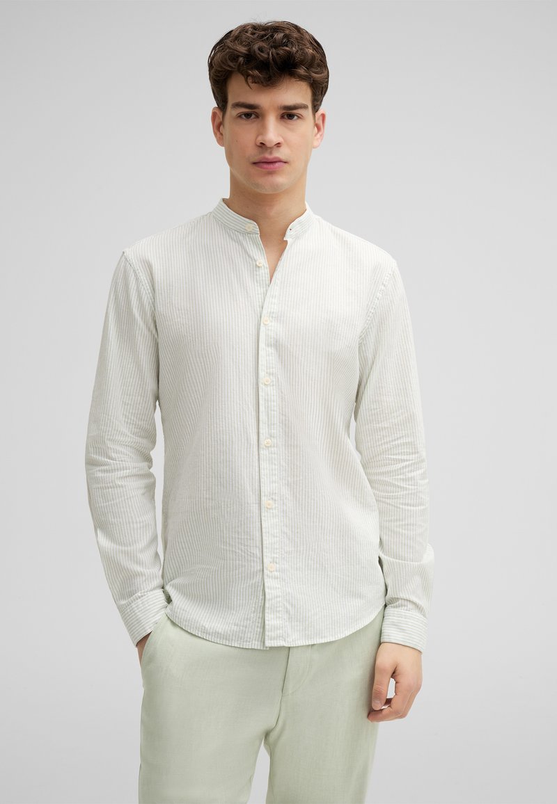 Helles gestreiftes Langarmhemd in hellgrün und creme, aus Baumwollstoff, mit Stehkragen, Knopfverschluss, schmale Passform, kombiniert mit hellgrünen Hosen.