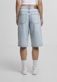 Lyseblå denimmekshorts med en afslappet pasform, der har baglommer og en brun lædermærke ved taljen. Hvide sneakers og sokker.