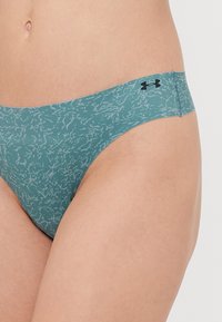 Teal madala tõusuga bikiinialuspesu, millel on peen abstraktne muster ja kontrastne must logo vööl. Sile kangastekstuuri.