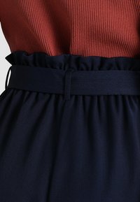 Ribbad rostorange topp med en marinblå kjol som har en volangmidja och ett matchande bälte, tillverkad av slät tyg med en strukturerad design.