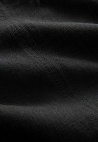 Tissu noir texturé avec une surface douce, présentant de fines lignes et un subtil éclat. Couture visible le long des plis, offrant un look polyvalent.