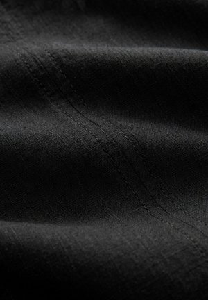 Tela negra texturizada con una superficie suave, que presenta líneas finas y un sutil brillo. Costuras visibles a lo largo de los pliegues, ofreciendo un aspecto versátil.