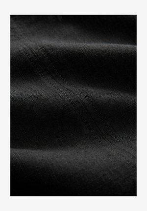 Tessuto nero con una superficie morbida, caratterizzato da linee sottili e una leggera lucentezza. Cuciture visibili lungo le pieghe, che offrono un aspetto versatile.