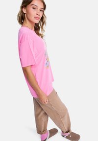 T-shirt oversize rose à manches courtes, avec un motif floral, assortie à un pantalon décontracté beige clair et des chaussettes roses.