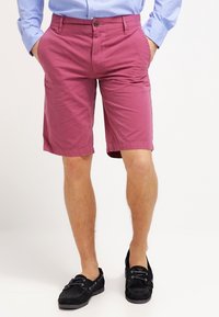 Pink cotton shorts with front pockets, a button closure, and belt loops, paired with black suede shoes.