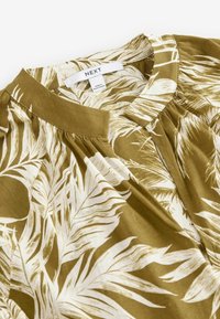 Olive green blouse with white leaf pattern, featuring a collar and pleated detailing. Made from lightweight fabric. Brand label visible.