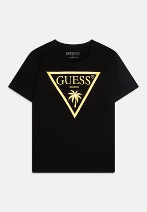 T-shirt noir à manches courtes avec un logo en forme de triangle jaune, les mots "GUESS," "BEACH," et un graphique de palmier au centre.