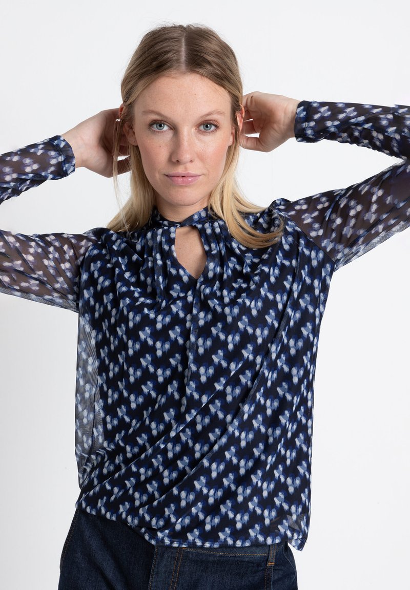 Marinebluse mit transparenten gemusterten Ärmeln, versehen mit einem Schlüsselloch-Ausschnitt und abstraktem blau-weißen Blumenmuster. Glattes Material, lockere Passform.