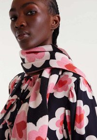 Bufanda multicolor con un patrón floral, con corazones rosas y rojos sobre un fondo negro, hecha de tela suave, drapeada alrededor del cuello.