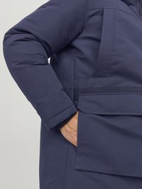 Giubbotto imbottito blu navy in tessuto resistente, con tasca frontale, dettagli cuciti e maniche con polsini.
