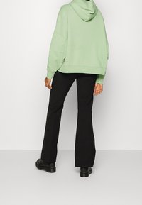 Sudadera oversized color verde menta con capucha, combinada con pantalones acampanados negros y zapatos gruesos negros, vista desde la parte trasera.