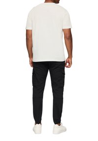 Witte katoenen t-shirt, korte mouwen, normale pasvorm, gecombineerd met zwarte cargobroek met zijzakken en elastische boorden. Gekozen met witte sneakers.