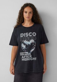 Czarny oversize t-shirt z graficznym nadrukiem dyskotekowej kuli i napisem: "DISKO DISKO WSZYSTKO DOBRE DZIEJE SIĘ PO PÓŁNOCY."