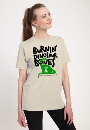 Licht beige t-shirt van katoen, met gedurfde zwarte tekst en een groene dinosaurusschaal. Het ontwerp bevat speelse tekst en een druip-effect.