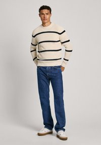 Maglione a righe crema con righe navy, aderente ai polsi, abbinato a jeans in denim blu e sneakers bianche con suole color cammello.