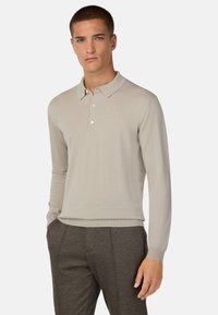 Jasnobeżowa, długosleeve polo z płaskim kołnierzykiem, trzema guzikami i ściągaczem u dołu, w połączeniu z szarymi, dopasowanymi spodniami.