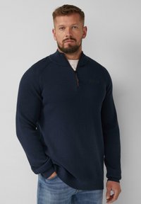 Marineblauer Strickpullover mit einem Viertelreißverschluss und hohem Kragen. Verfügt über eine gerippte Textur, seitliche Schlitze und ein Logo-Patch auf der Brust.