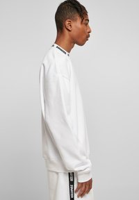 Hvid sweatshirt lavet af blødt stof, med en ribbet krave og sort "STARTER" logo, dropped shoulders og en afslappet pasform.