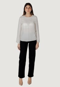 Blusa bianca a maniche lunghe in tessuto texturizzato, con delicati motivi, abbinata a pantaloni neri a gamba dritta e tacchi color nude.