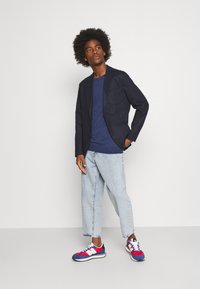 Navy blazer with a single front pocket, dark blue t-shirt, light wash cropped jeans, and multicolored sneakers with red, blue, and white accents.