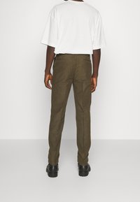 Olivgröna byxor i bomullsmix med rak bendesign, två bakfickor och en ren finish. Bärs med en vit T-shirt.