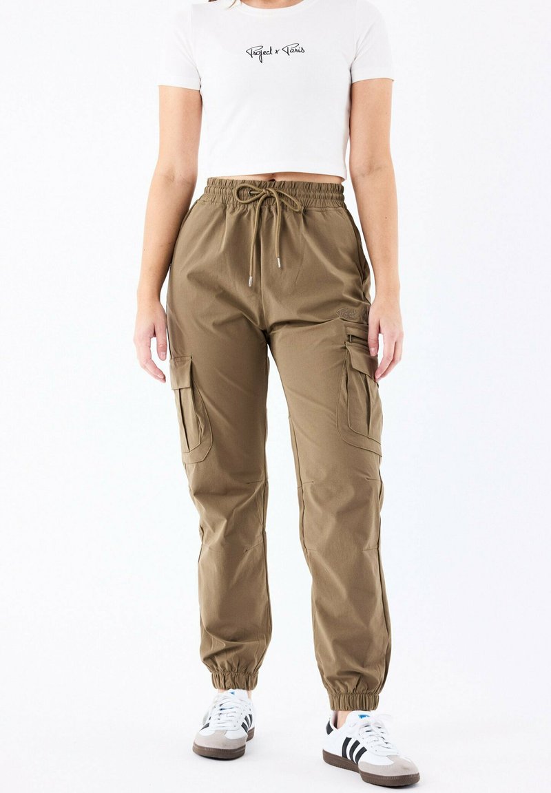 Pantalones cargo marrones con puños y cintura elásticos, que presentan múltiples bolsillos laterales y una textura de tejido suave. Combinados con una camiseta corta blanca.