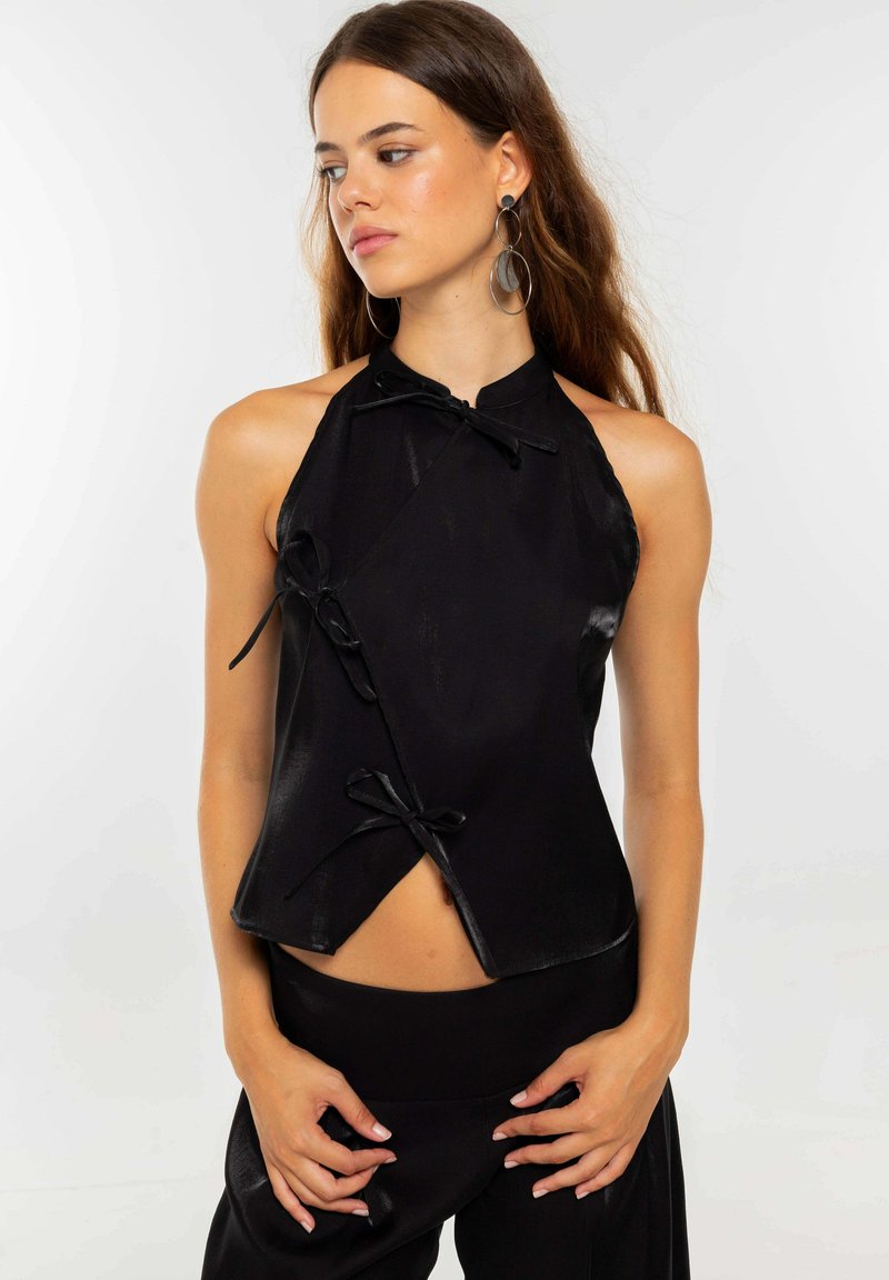 Top halter negro de satén, con un diseño cruzado único que incluye lazos decorativos y un ligero brillo. Textura suave con un ajuste entallado.