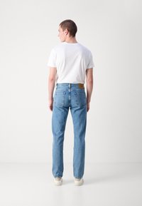 Jeans din denim de culoare albastru deschis, cu croi drept și talie înaltă, având două buzunare spate și o etichetă din piele maro cu brandul. Purtați cu un tricou alb.
