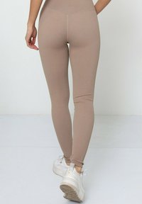 Leggings beiges côtelés avec une taille haute et une coupe ajustée, associés à des baskets blanches. Le tissu semble extensible et texturé.