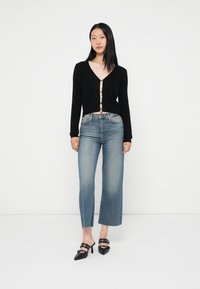 Svart kort cardigan med V-hals och knappdetalj, parat med högmidjade, ljusblå vida jeans och svarta klackskor.