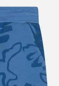 Blaue Jogginghose mit einem tonalen, abstrakten Muster, ausgestattet mit einem gerippten Bund und einer glatten, weichen Stofftextur. Strapazierfähige Nähte.