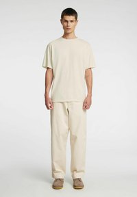 Beżowa bawełniana koszulka z okrągłym dekoltem i luźnym krojem, w połączeniu z pasującymi beżowymi spodniami o szerokich nogawkach oraz jasnymi butami.