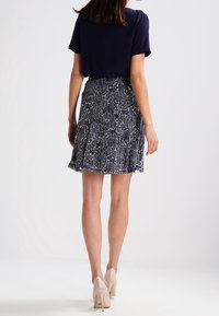 Laivastonsininen yläosa yhdistetty valkoisin kukkakuvioin koristettuun polvipituiseen kuviolliseen hameeseen; sileä kangas, jossa hienovarainen liehuvuus. Beigejä korkokenkiä täydentämään asua.