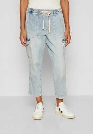 Person wearing light blue cropped denim cargo pants with drawstring waist and white sneakers with black accents.