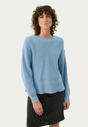 Pull en maille bleu clair avec une texture côtelée, col rond et fentes latérales. Associé à une jupe en denim foncé.