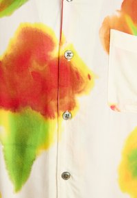 Camicia a maniche corte in tessuto leggero con base crema e grandi motivi astratti rossi, arancioni e verdi. Inclusi bottoni e taschino sul petto.