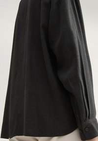 Black long-sleeve shirt with a relaxed fit, featuring button cuffs and a soft, textured fabric. Displays a side view emphasizing the sleeve.