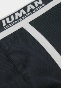 Czarna prążkowana męska bielizna z białym paskiem, z wyraźnym napisem marki "Intimissimi Uomo". Miękka tekstura, dopasowany krój.