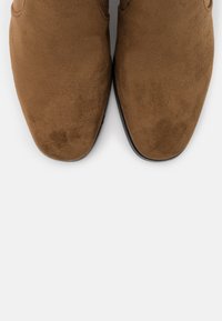 Hnědé semišové boty s hladkým povrchem a zaoblenou špičkou. Elegantní design s jemným leskem a minimalistickým stylem.