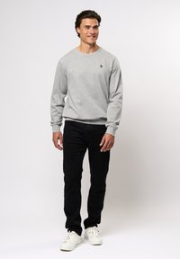 Grijze sweatshirt van zacht katoen met lange mouwen, ronde hals en klein logo op de borst, gecombineerd met zwarte broek en witte sneakers.